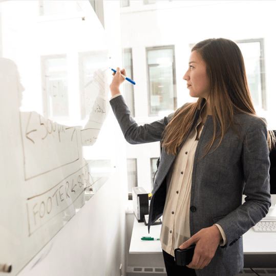 alt="A woman writing on a whiteboard during an office presentation."